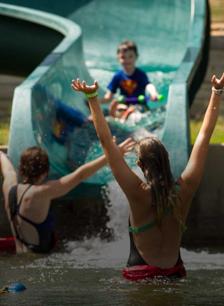 Camp counselors helping camper go down slide